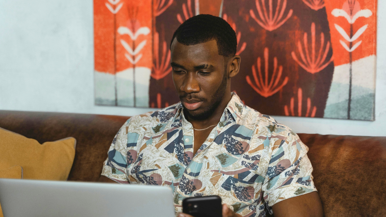 African gig worker looking at laptop and phone
