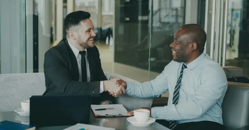 Two professionals shaking hands across a meeting table, illustrating the trust that selling African talent globally depends on.